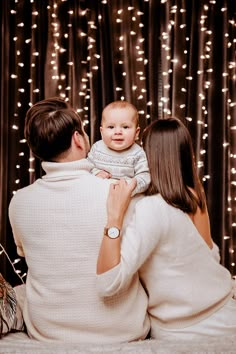 a man and woman holding a baby in front of a backdrop with lights on it