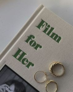 two gold hoop earrings sitting on top of a book with the title film for her