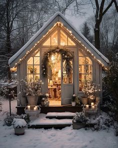 a small white house is lit up with christmas lights and wreaths in the snow