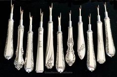 seven silver spoons lined up in a row on a black surface with ornate designs