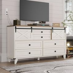 a large flat screen tv mounted on top of a white dresser in a living room