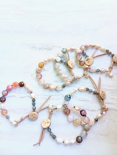 These bracelets feature a combination of polished and faceted beads in soft, pastel shades, including whites, greens, champagne, pinks, orange, coral, purple, and blues. Made of stunning Opals, Moonstone, Ruby Agate, matte Frost Agate cubes, Tibetan Agate, AAA Labradorite, Ocean Jasper, and an artistic array of pastel, champagne, and alabaster Fresh Water Pearls. Gold accents and small spacer beads are also used to add subtle elegance. The overall design is earthy and delicate, blending natural materials with a refined aesthetic. Unique beige suede and wood button closure, give a rustic edge. Strung on Beadalon .015 7-strand Stainless Steel Bead Stringing wire-great strength and great flexibility. The item/s pictured is the item you will receive. Bracelet is 7.0 to 7.5" in length. Everyday Agate Beaded Bracelets, Everyday Agate Beaded Bracelet, Everyday Beaded Agate Bracelets, Everyday Hand-strung Agate Beaded Bracelets, Bracelets Pearls, Subtle Elegance, Orange Coral, Fresh Water Pearls, Pastel Shades