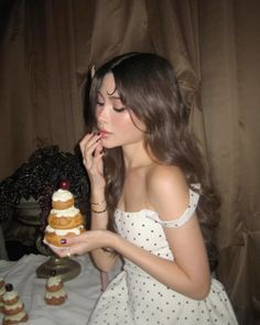 a woman in a white dress is holding a cake and looking down at the camera