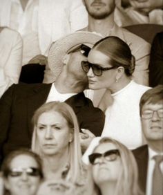 two people kissing each other in front of a crowd at a tennis match, with one person wearing sunglasses and the other looking down