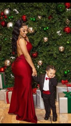 a woman in a red dress standing next to a little boy wearing a tuxedo