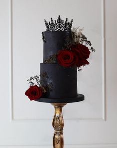 a three tiered black cake with red roses on the top and gold decoration around it