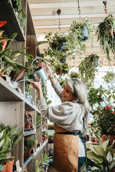 a woman is watering plants in a flower shop with lots of potted plants on shelves