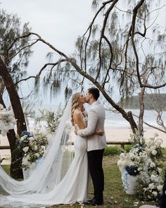 a bride and groom kissing in front of an outdoor wedding ceremony arch with white flowers