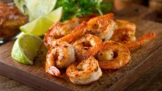 some shrimp on a wooden cutting board with limes and cilantro in the background