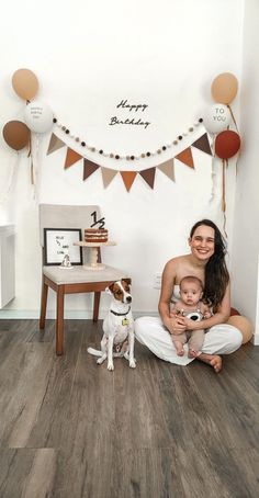 a woman sitting on the floor with her baby and dog in front of a happy birthday banner