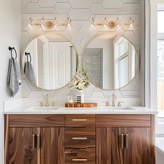 a bathroom with two round mirrors on the wall and wooden cabinets in front of it