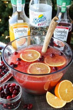 a glass bowl filled with oranges and cranberries next to bottles of alcohol