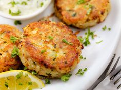 three crab cakes on a white plate with lemon wedges and parsley garnish