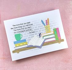 a card with an open book and some books on a shelf next to a cup