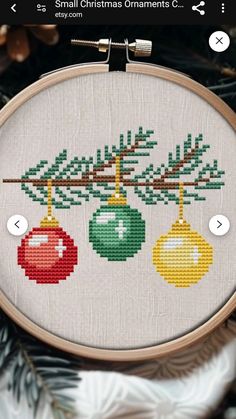 a cross stitch christmas ornament hanging from a tree with baubles on it