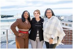 three women standing next to each other on top of a building