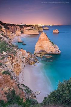 the beach is surrounded by rocky cliffs and blue water at dusk, as seen from above