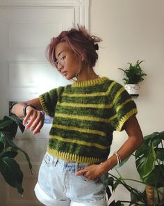 a woman standing next to a potted plant wearing a green and yellow striped sweater