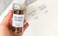 a hand holding a jar filled with crushed pepper next to a piece of white paper