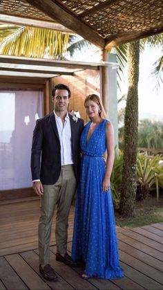 two people standing next to each other on a wooden deck with palm trees in the background