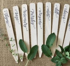 six wooden spoons with writing on them sitting next to some green leaves and flowers