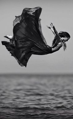 a woman flying through the air while wearing a long black dress with her arms outstretched