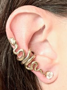 This Snake Ear Cuff is cast in solid 14K gold. The graceful snake wraps playfully along the edge of the ear. It can be worn on either the left or the right ear. (Diamond not included.)Our ear cuffs require no piercings. Starting near the top of the ear, slide the ear cuff down along the edge of the ear's cartilage. You may gently open or close the opening of the ear cuff to accommodate the thickness of your ear.This item usually ships the same or next business day.All Marty Magic Jewelry is pack Unique Gold Pierced Ear Climbers, Adjustable Gold Clip-on Jewelry, Snake Ear Cuff, Jóias Body Chains, Serpent Jewelry, Snake Ears, Ear Cuff Jewelry, Bar Stud Earrings, Snake Jewelry