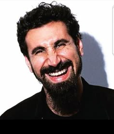 a man with a beard smiling and wearing a black shirt in front of a white wall