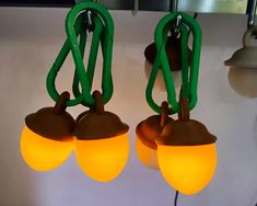 three green and yellow lights hanging from hooks on a white wall with a light fixture in the background