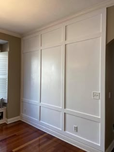 an empty room with white paneling and wood floors