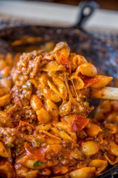 a wooden spoon full of pasta and meat in a skillet on top of a stove