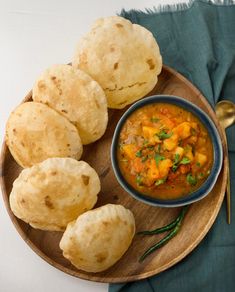 a wooden plate topped with dumplings and a bowl filled with stew next to it