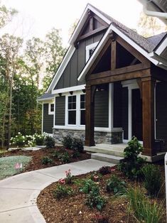 a small gray house with white trim and wood accents on the front porch, along with stone steps leading up to it