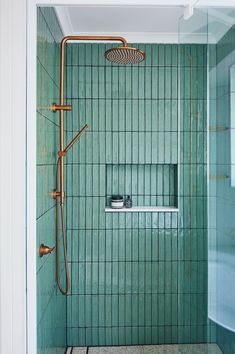 a green tiled shower in a bathroom with copper fixtures and hand held showerhead,