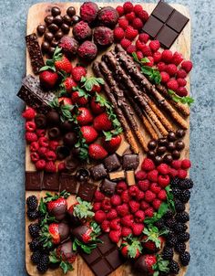 an assortment of chocolates, strawberries and berries on a cutting board with mint leaves