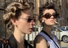 two women standing next to each other in front of a building