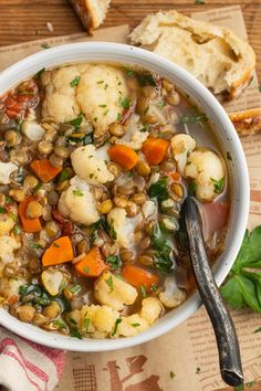 a white bowl filled with vegetable soup on top of a wooden table next to bread