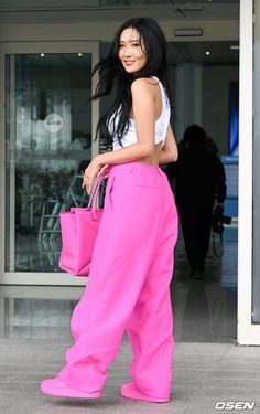 a woman with long black hair wearing pink pants and holding a pink bag in her hand