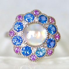 Rainbow Moonstone Sapphire Halo Gold Ring Pink and Blue Sapphire Edwardian Style moonstone Ring wedding Engagement Ring. Rainbow Moonstone Sapphire Halo Ring Pink and Blue Sapphire  Edwardian Style moonstone Ring wedding Engagement Ring. 14K White Gold US7 This cocktail ring features my mini cocktail ring designed with one piece of rainbow color  moonstone cabochon and a fancy double halo of cornflower blue sapphire and pink sapphires! The size is in US 7 made of solid 14K white gold can be size White Multi-stone Moonstone Ring, Unique Blue Cabochon Moonstone Ring, Unique Blue Moonstone Cabochon Ring, Blue Moonstone Wedding Ring Birthstone, Multi-stone Moonstone Ring For Anniversary, Blue Moonstone Ring With Accent Stones For Anniversary, Blue Moonstone Ring With Accent Stones, Unique Blue Moonstone Ring, Blue Multi-stone Opal Ring For Wedding