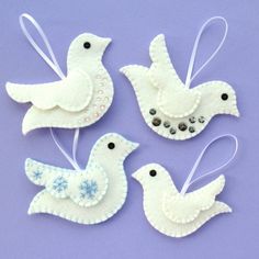 four white felt birds are hanging from strings on a purple background with beads and sequins