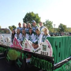 a group of people riding on the back of a green and white float in a parade