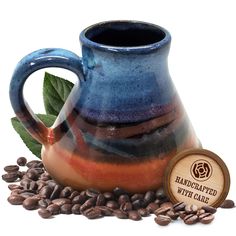 a blue and brown ceramic coffee pot sitting on top of beans with a label that says handcrafted with care