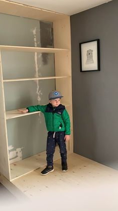 a young boy standing in front of a book shelf with his hands on the shelves