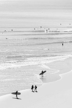 black and white photograph of people walking on the beach with their surfboards in hand