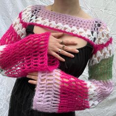 a woman wearing a pink and green crochet sweater with her hands on her chest