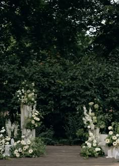 an outdoor ceremony setup with white flowers and greenery on the ground, surrounded by tall trees