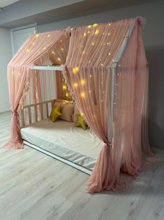 a canopy bed with pink curtains and lights on the ceiling is in a room that has white wood flooring