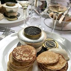 some pancakes are on a white plate with silverware and wine glasses in the background