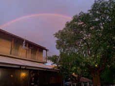 a double rainbow is seen over a house in the evening hours as people walk by