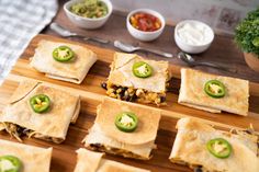 several quesadillas are arranged on a cutting board with green peppers and salsa